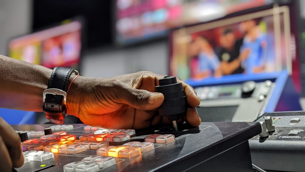 Operator using a broadcast control mixer with multiple video screens, illustrating the production of sports feeds, commentary, and analysis.